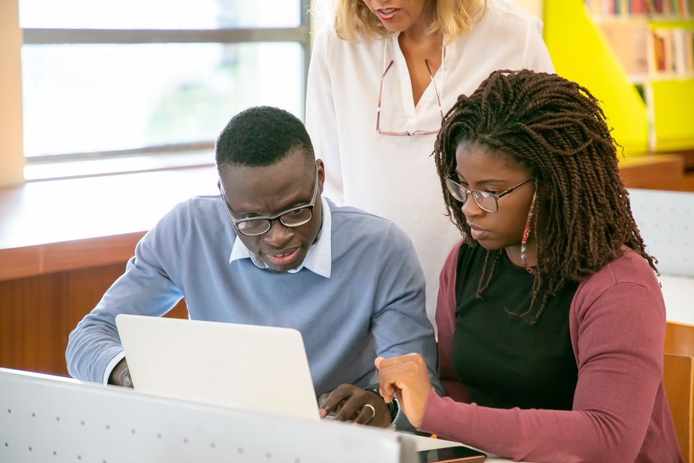 Un étudiant et une étudiante travaillent ensemble sur un ordinateur, guidés par un aîné